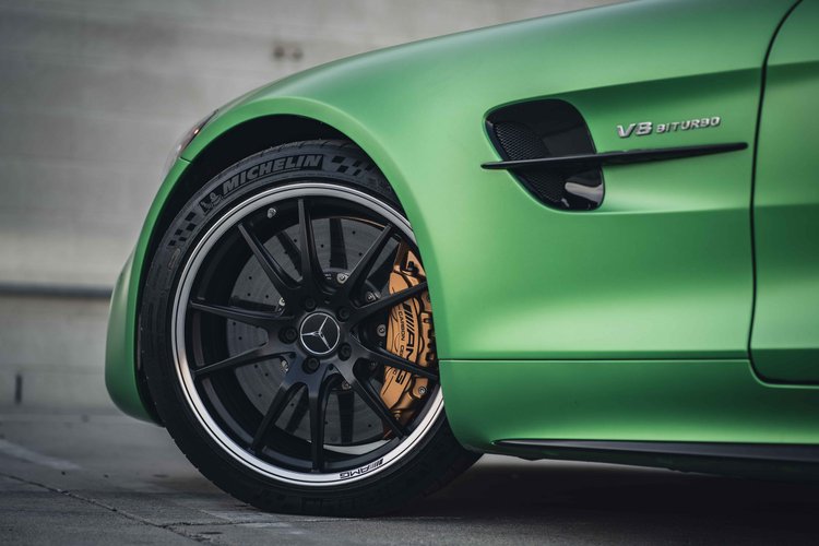 Dark front wheel with a silver rim edge and gold-toned caliper beside the black fender vent and green side panel.