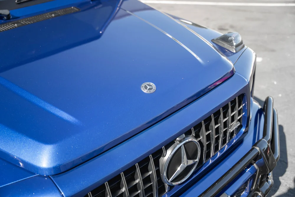 High blue G 63 hood close-up with a round Mercedes badge, vertical grille bars and dark front guard