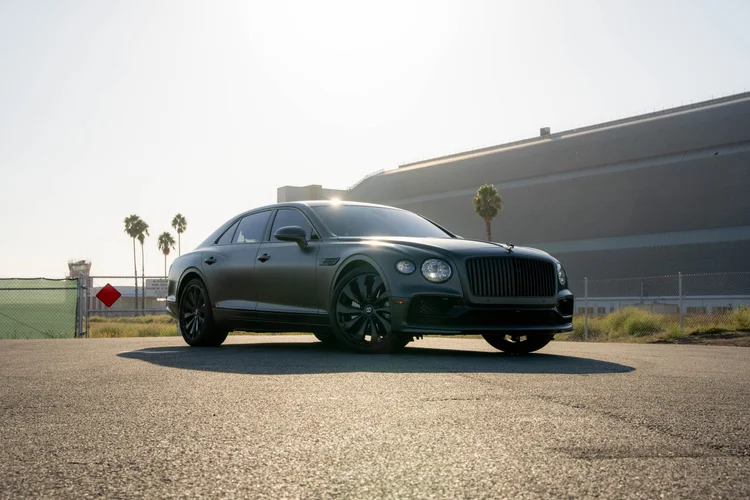 Complete low front-corner view of the gray sedan with sunlit roof and dark wheels.