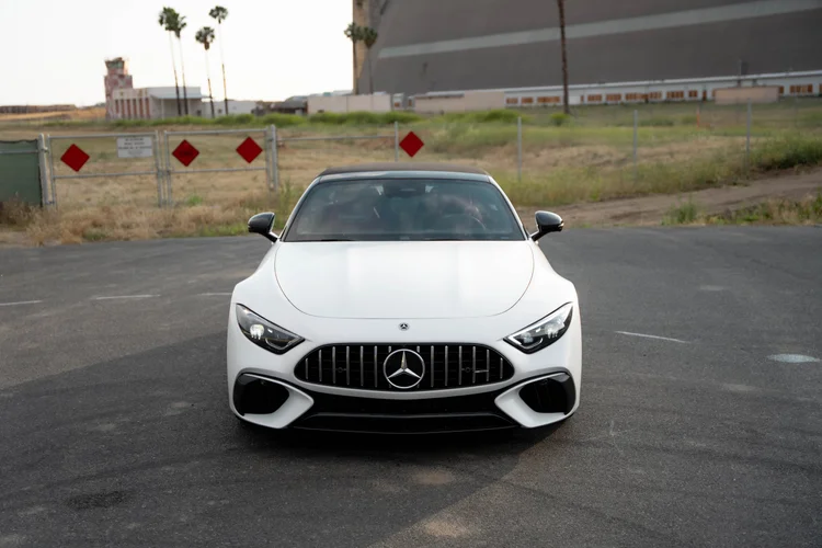 Complete high frontal view of the white SL 63 centered on pavement below a fence with red diamond-shaped signs