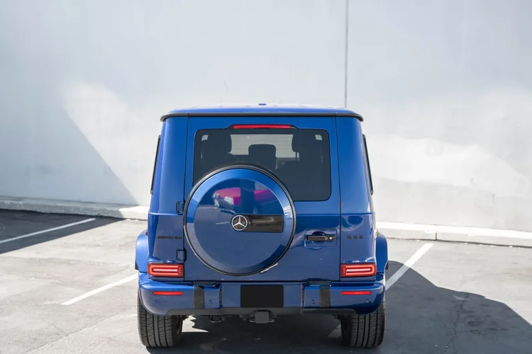 Complete high rear view of the blue G 63 showing its roof, dark rear glass, red lamps and round spare-wheel cover