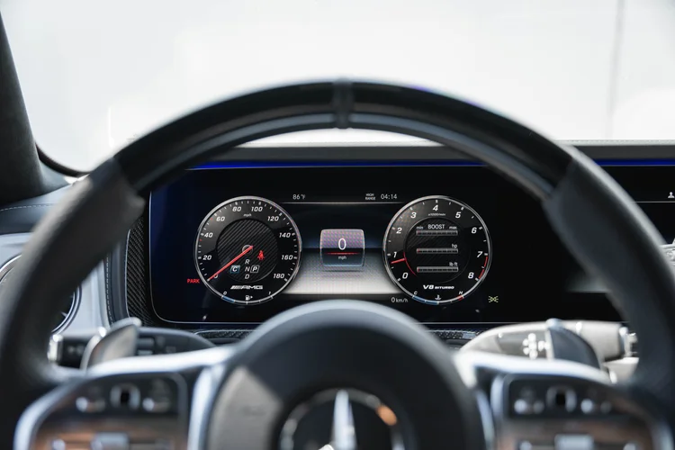 Digital instrument display with round gauge graphics and a blue-lit dashboard edge viewed behind the G 63 steering wheel
