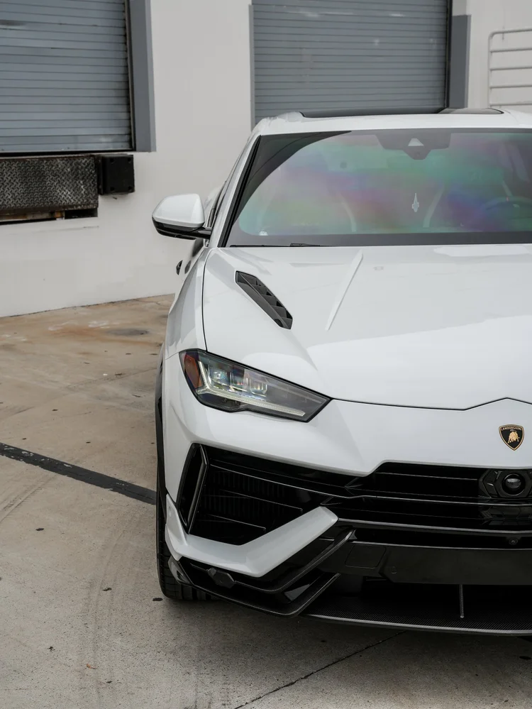 Close partial front view showing a white mirror, windshield, hood vent, headlamp and black front intake trim.