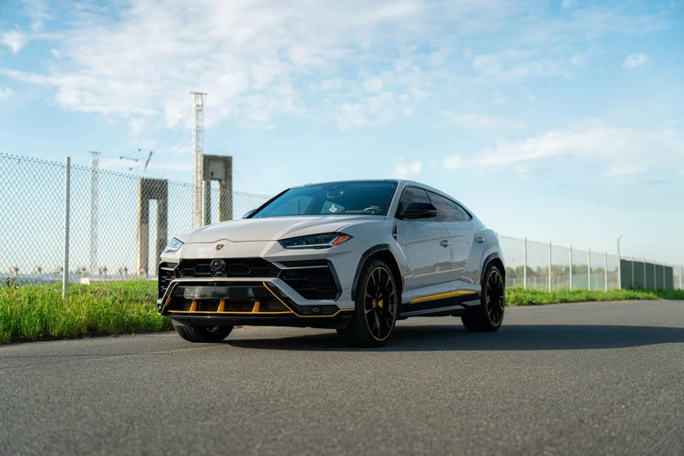 Light-colored Lamborghini Urus in a complete front three-quarter view with dark wheels and yellow lower accents.