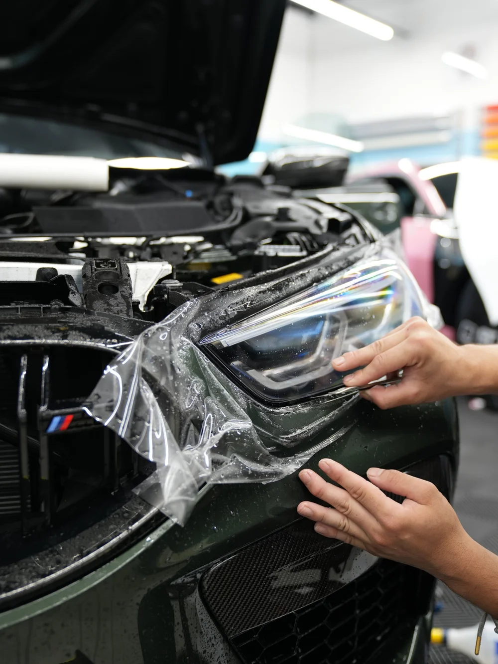 Paint protection film being fitted around a black BMW headlight
