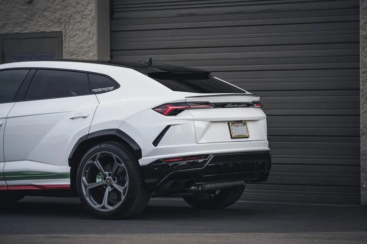 Wide partial rear three-quarter view with a gray rear wheel, red lamps, dark lower bumper and striped lower side.