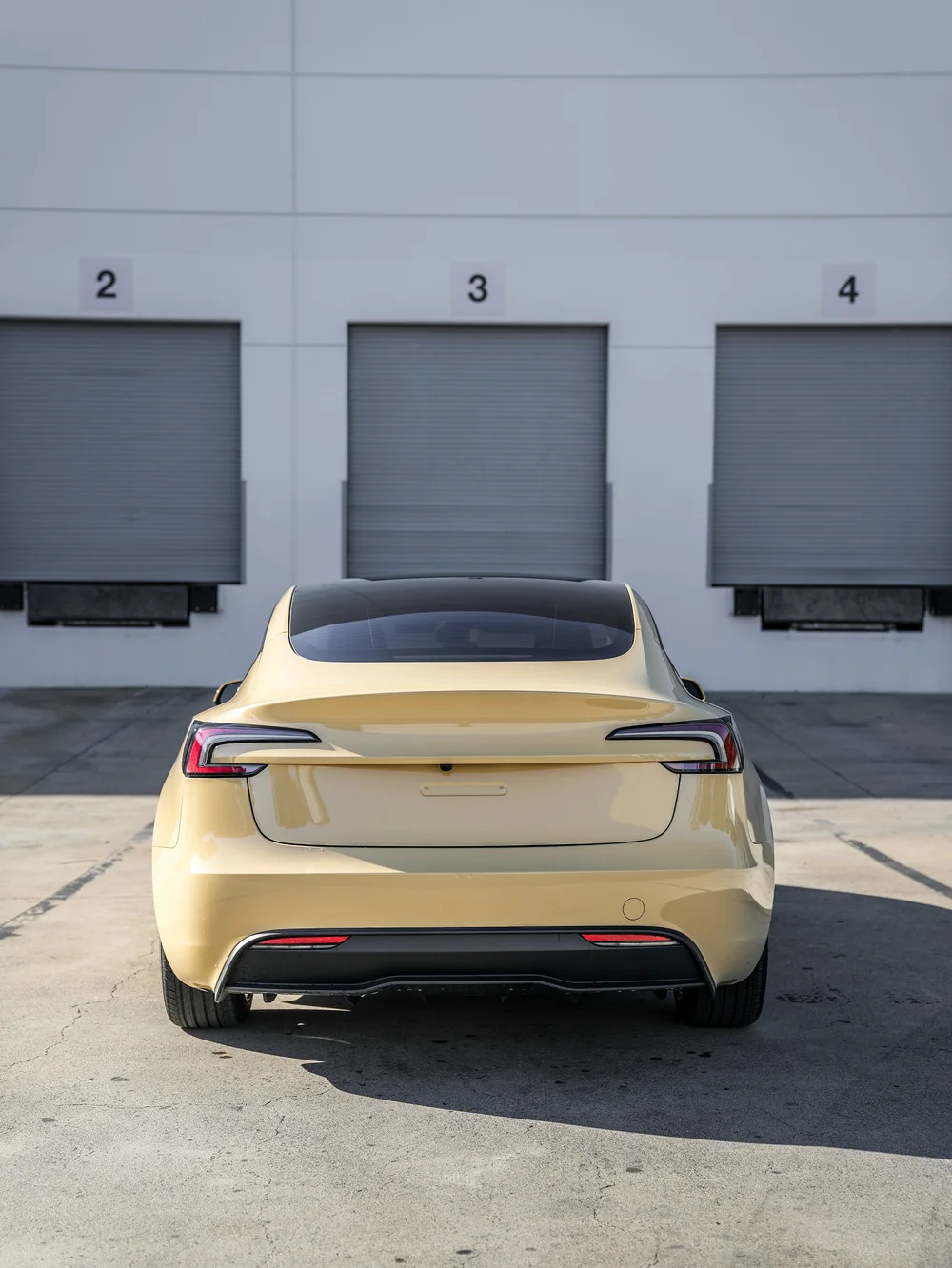 Tesla Model 3 in gloss Sunrise Yellow vinyl wrap, straight rear view of the complete vehicle