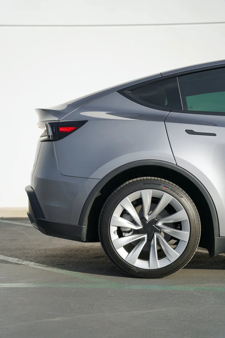 Close-up of the Tesla Model Y rear wheel, tyre, gray rear quarter panel, side glass and door handle.