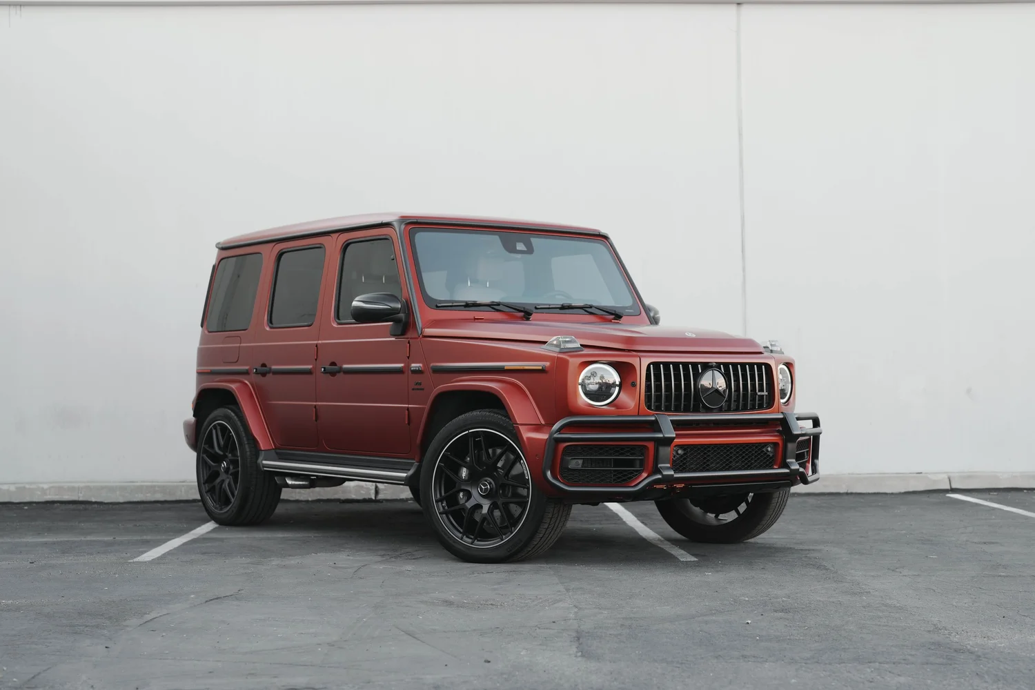 Complete front three-quarter landscape of the matte red G63 with round headlights, vertical grille and front bumper guard