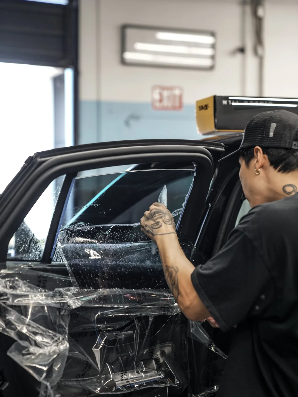 Technician working with a flat hand tool at wet side-window film on an open Mercedes-AMG GLC 63 S door, with a transparent protective cover across the door trim.