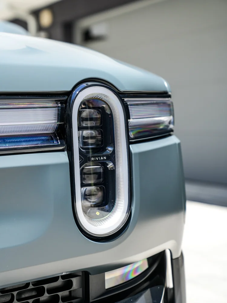 Close view of a Rivian R1T oval headlamp, horizontal front light strip and satin bodywork.