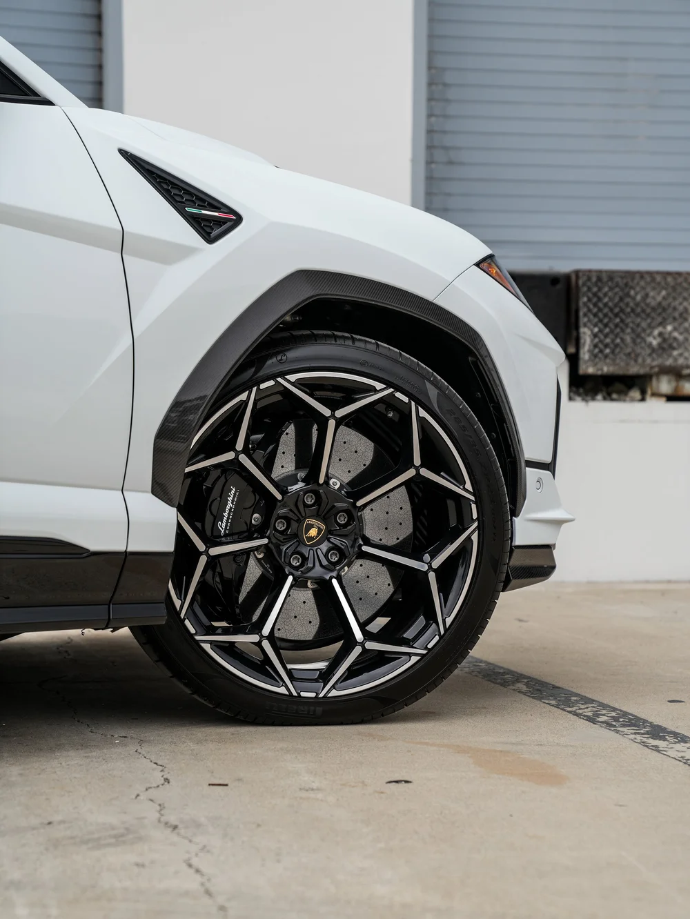 Black-and-silver front wheel beneath a woven-pattern arch trim, with a drilled brake disc and Lamborghini lettering on the caliper.