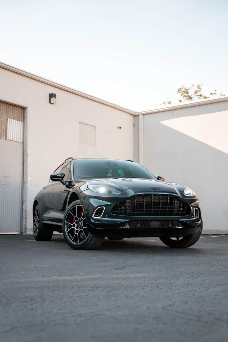 Front corner portrait of the green SUV with wall and sky surrounding it.