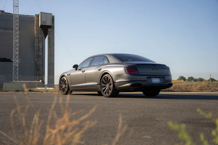Complete rear-three-quarter view of the long gray sedan with dry grass in the foreground.