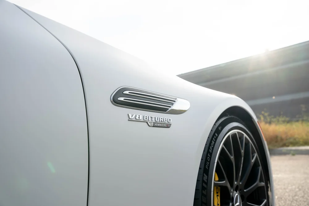 Literal V8 BITURBO and 4MATIC+ lettering below the bright fender trim on the white SL 63 beside part of a dark front wheel