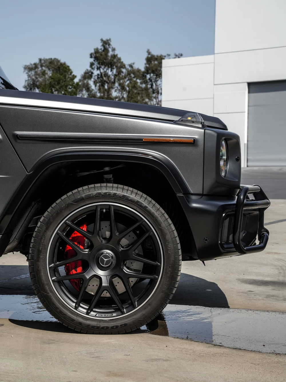 Black front wheel and red brake caliper beneath the satin grey Mercedes-AMG G 63 fender and amber side reflector