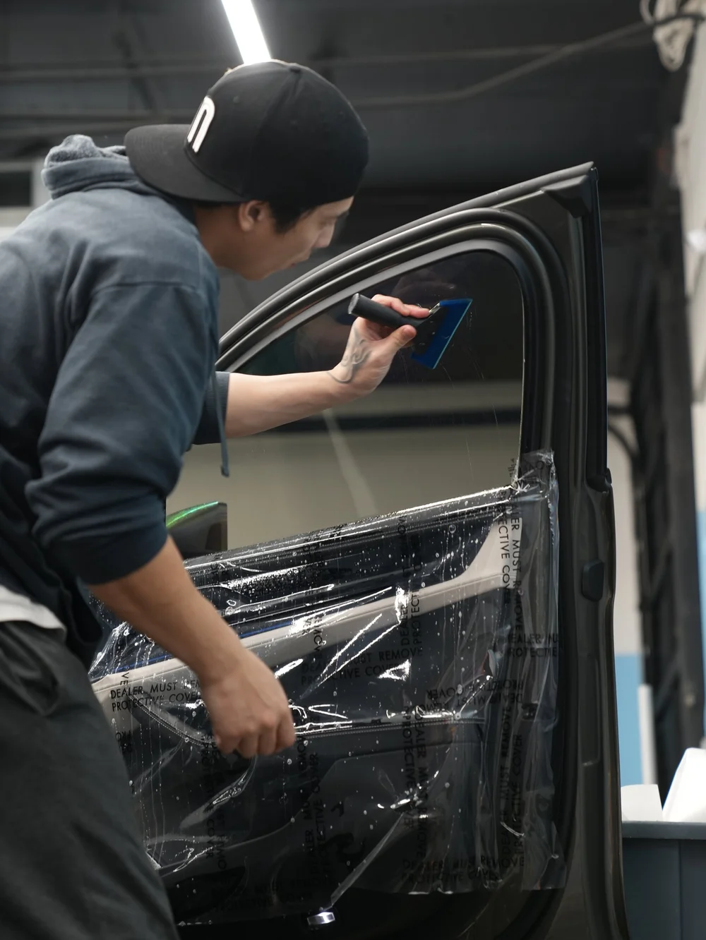 Blue squeegee working across wet side glass with the door open and nearby trim covered