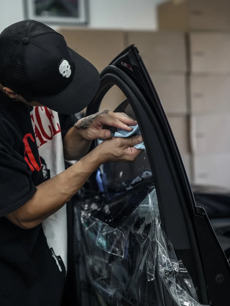 Technician holding a blue cloth against the upper side-window area of the Mercedes-AMG GLC 63 S, with an open door and a transparent protective cover over the trim.