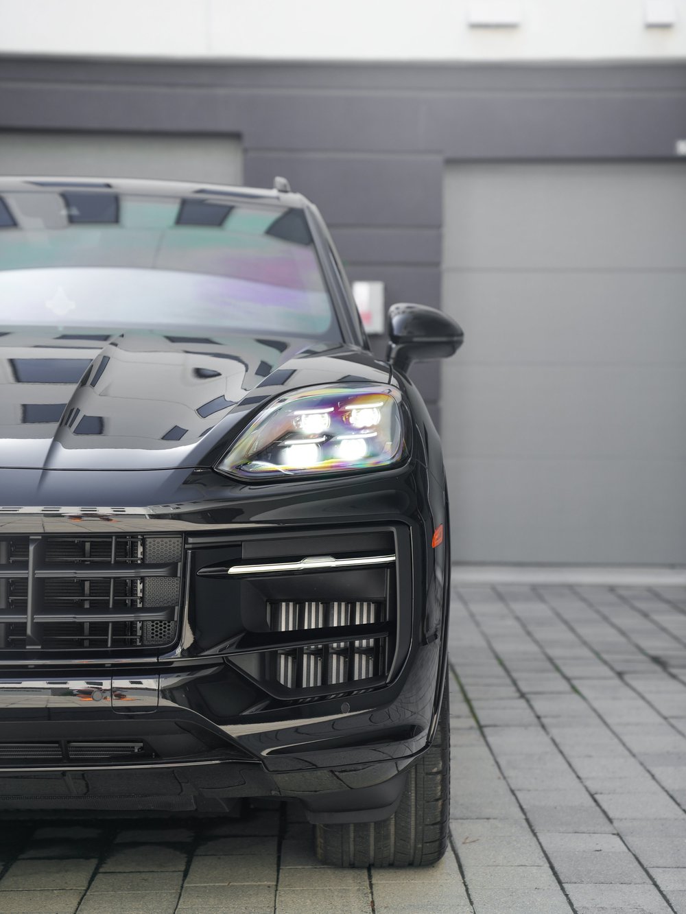 Close view of one Cayenne GTS headlamp, glossy bonnet, front grille, bumper and adjacent tyre.