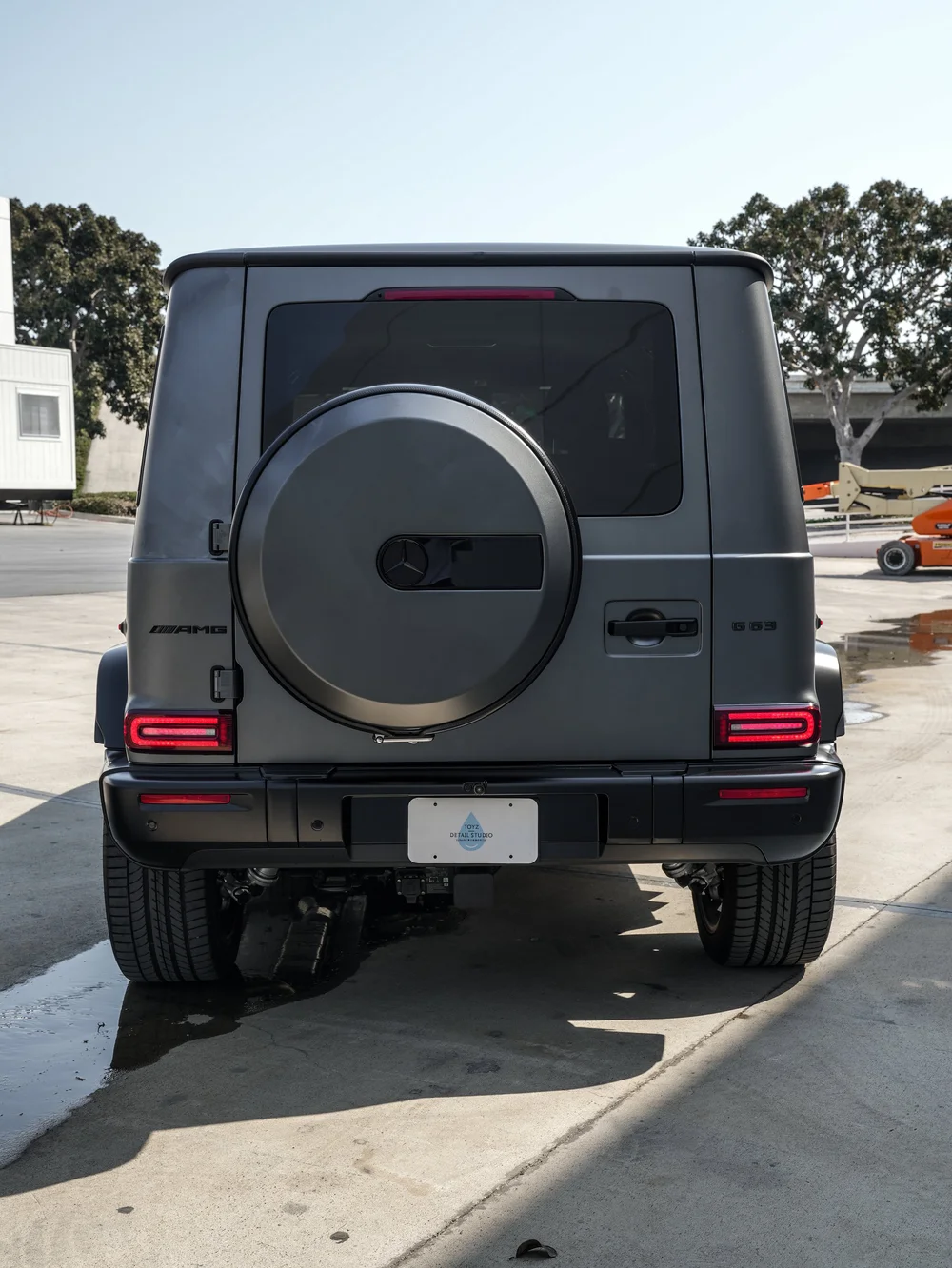 Straight-on rear view of the satin grey Mercedes-AMG G 63 with spare-wheel cover, dark rear glass and red taillamps