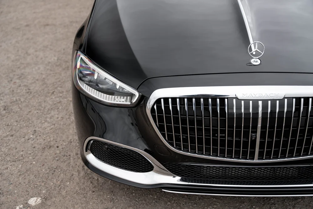 High front detail of the black hood and Mercedes ornament above a headlamp and bright MAYBACH-lettered grille surround