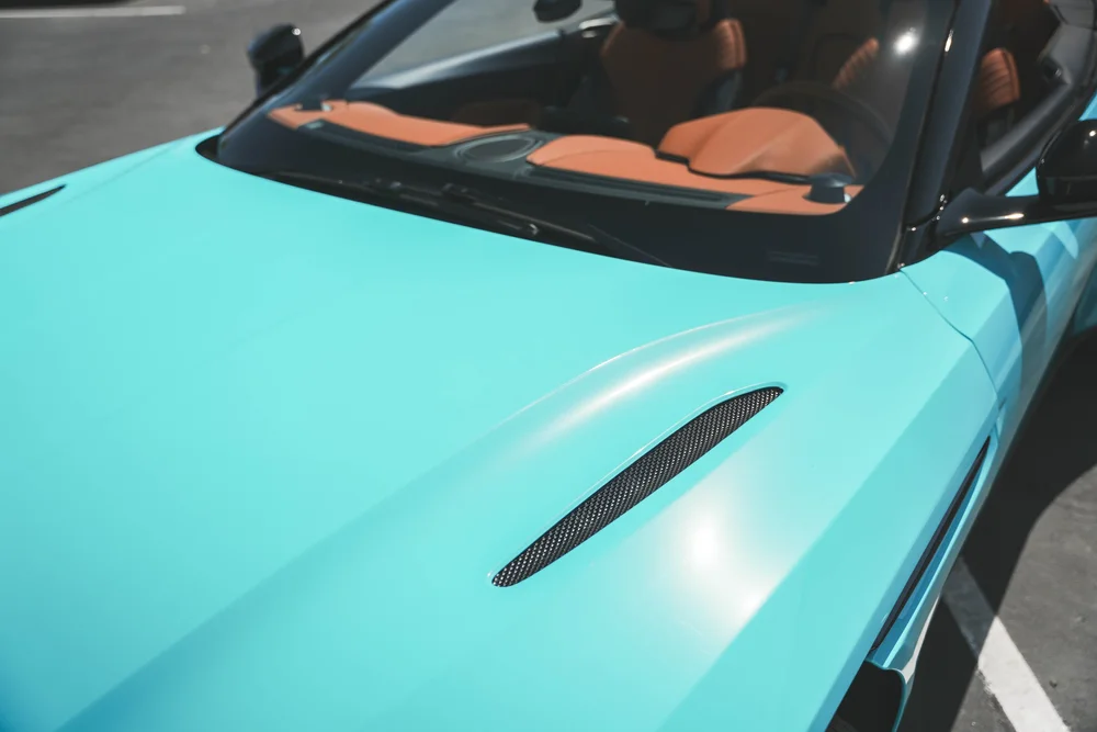 Miami Blue DB11 hood ridge and black mesh vent leading toward the windscreen and orange open-roof cabin
