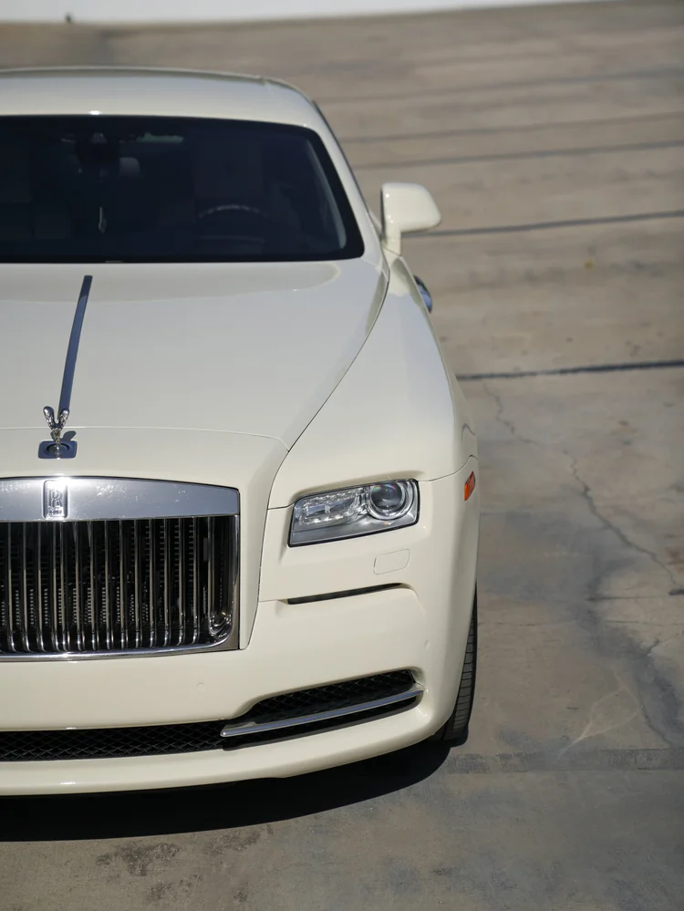 High partial front view of the Rolls-Royce Wraith showing the pale hood, ornament, headlamp and grille.