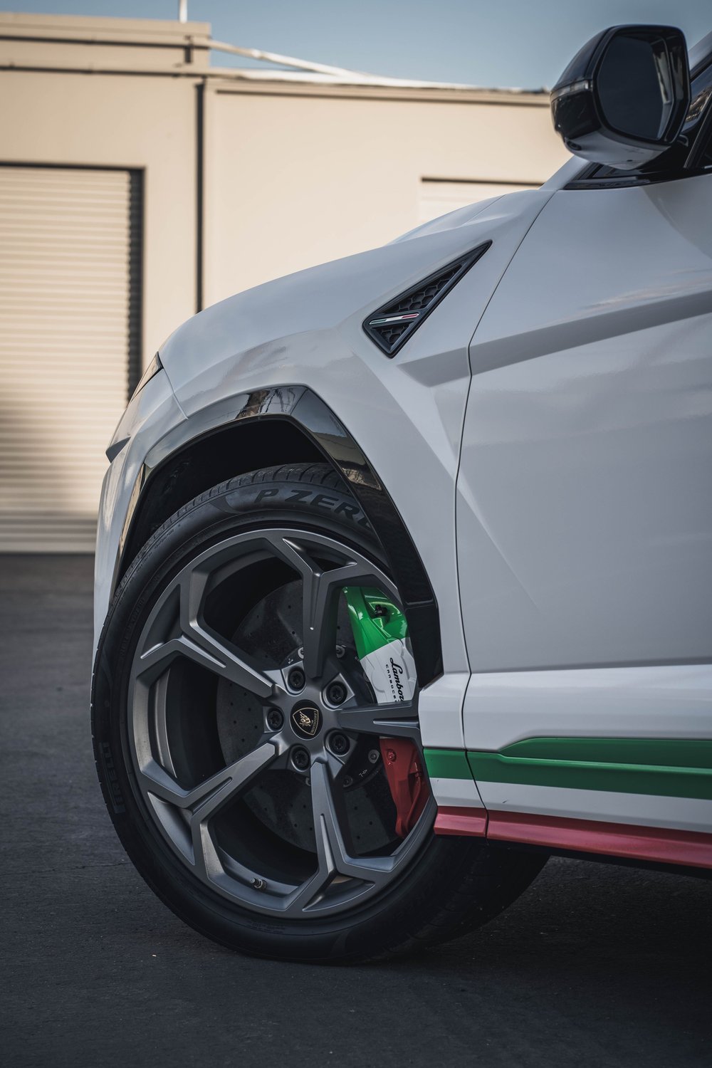 Gray front wheel and green, white and red caliper beside matching lower-side bands, a white fender and dark mirror.