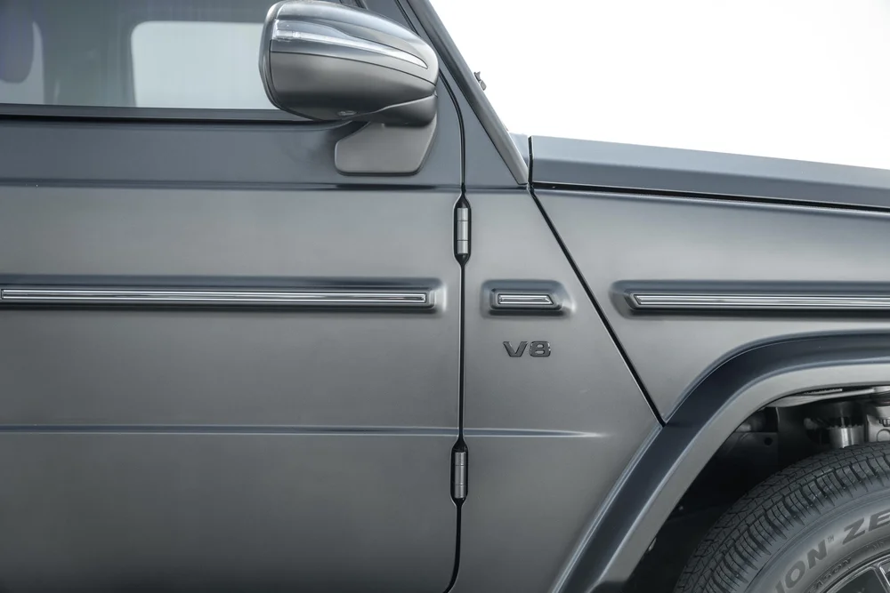 Close side detail of the grey G 550 mirror, exposed door hinges, bright trim strip and V8 fender lettering
