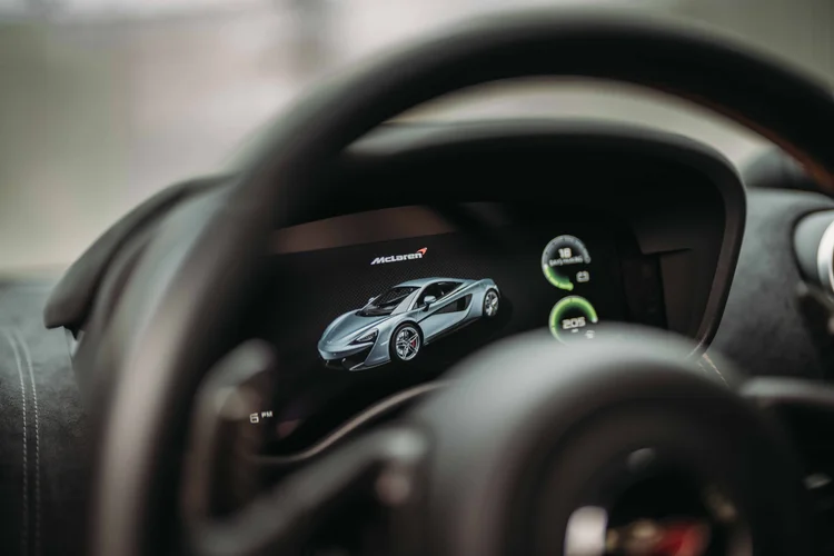 Instrument display showing a car graphic behind the out-of-focus steering wheel.
