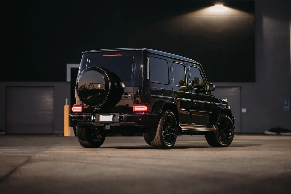 Complete rear three-quarter view of the dark G 63 beneath the building light, showing black wheels and red rear lamps.