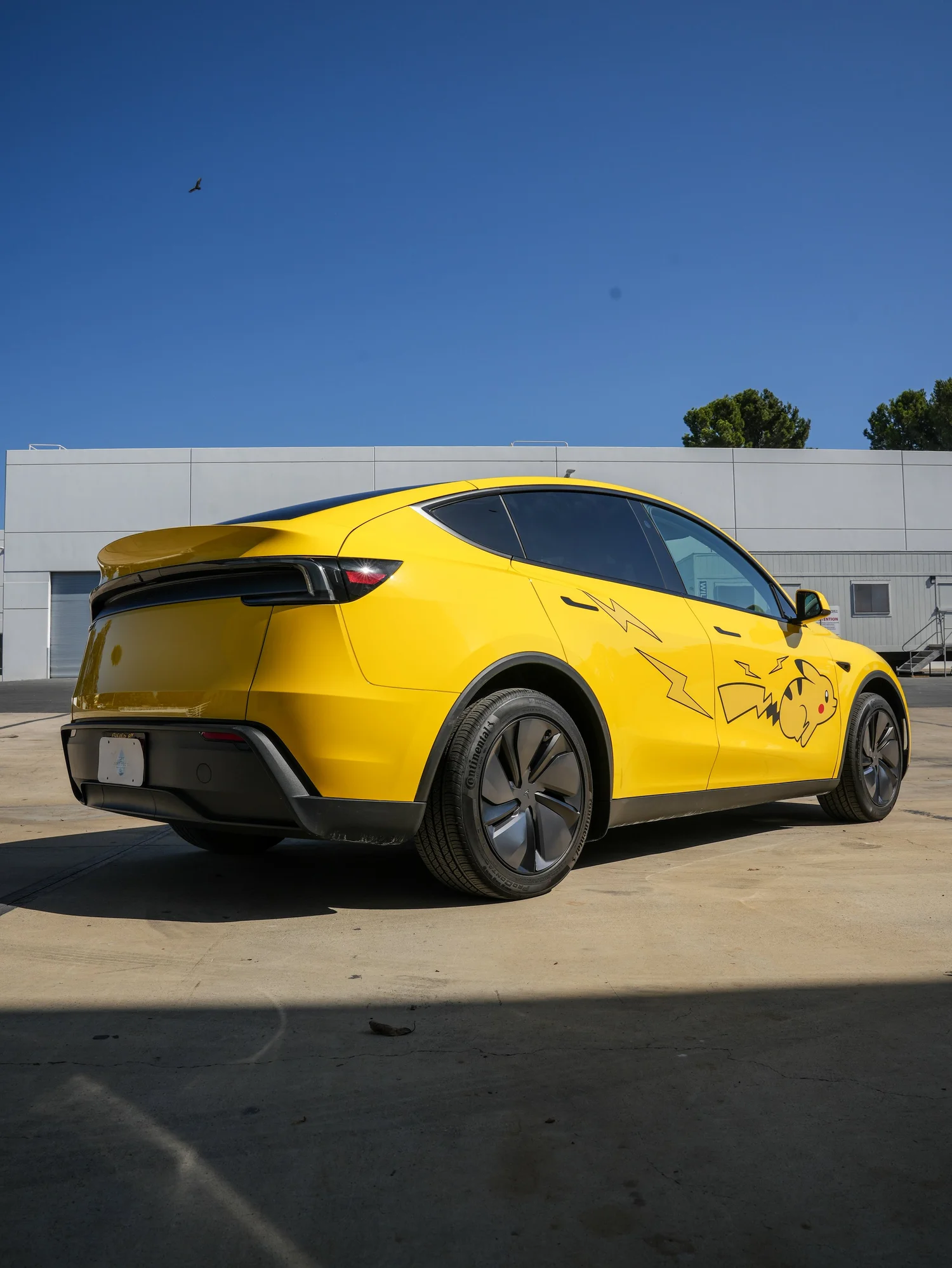 Tesla Model Y with Vegas Yellow vinyl wrap and Pikachu graphics, rear three-quarter view