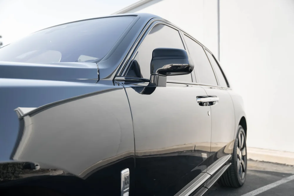 Dark Metallic Grey Rolls-Royce Cullinan — side glass, mirror and exterior-panel reflections in a low landscape detail