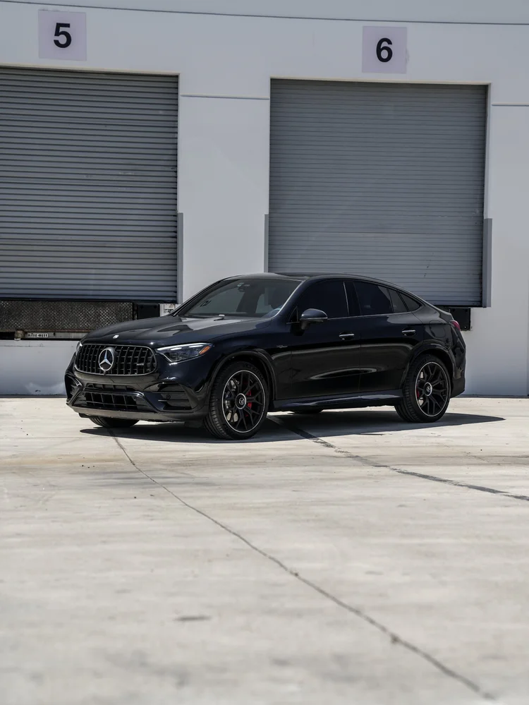 Complete wider front three-quarter view of the black Mercedes-AMG GLC 63 S facing left, with dark wheels, red brake calipers and dark side glass outside numbered workshop doors.
