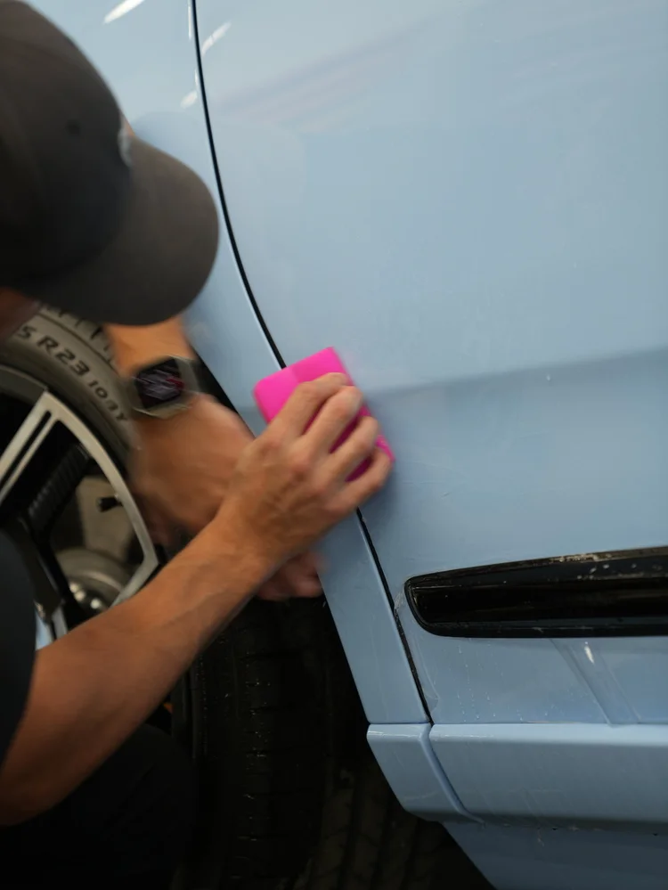 Technician smoothing clear film on the Powder Blue Cullinan side panel near a wheel and dark lower trim