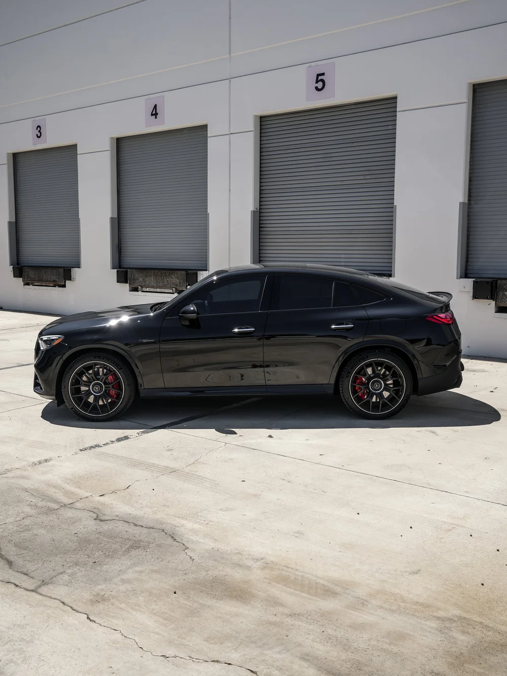 Complete left-facing side profile of the black Mercedes-AMG GLC 63 S, showing its sloping rear roofline, dark side glass, multi-spoke wheels and red brake calipers.