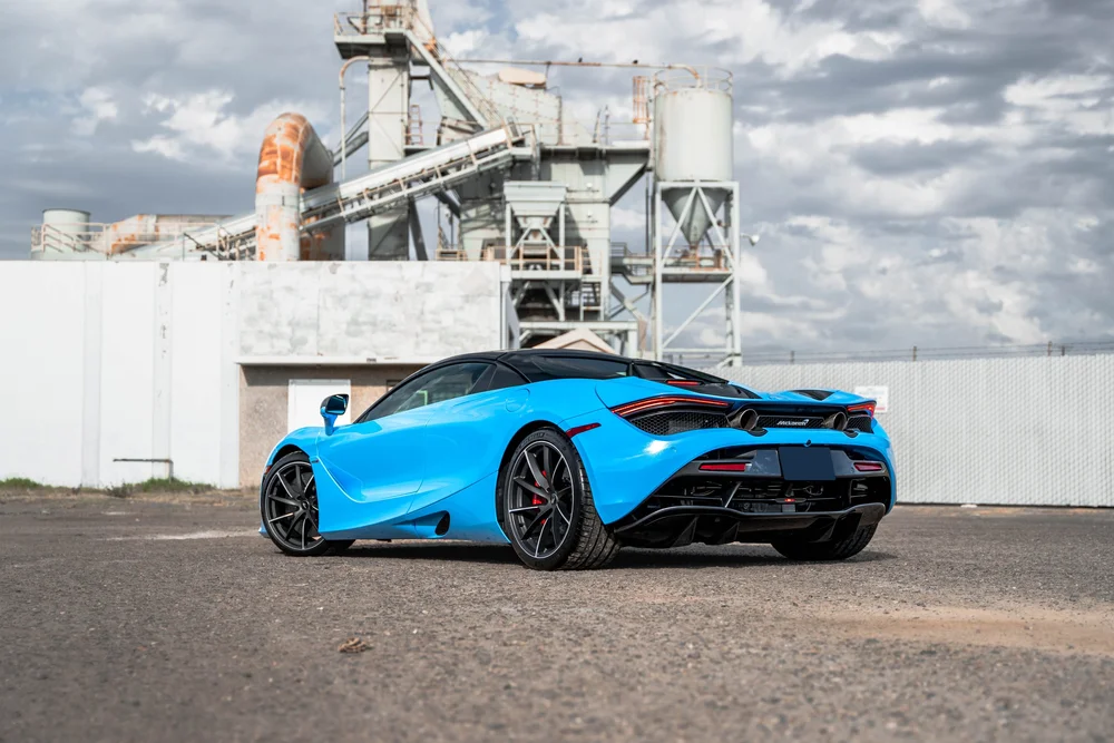 Blue McLaren 720S in a wide rear three-quarter view beneath a cloudy sky