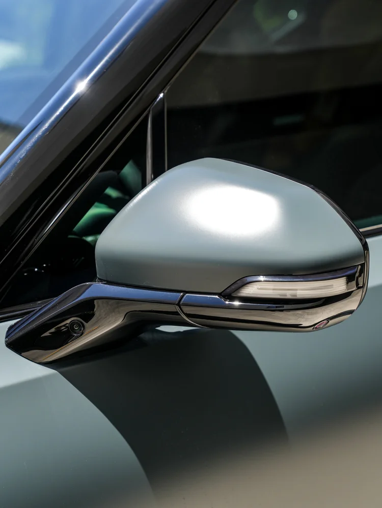 Rivian R1T side-mirror detail showing a satin upper housing, black lower trim and lamp strip beside the side glass.