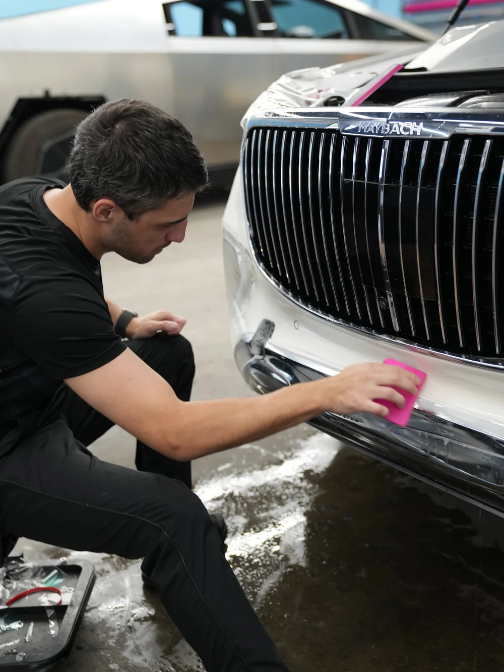 Pink squeegee smoothing wet clear film across the white front bumper below the MAYBACH grille.
