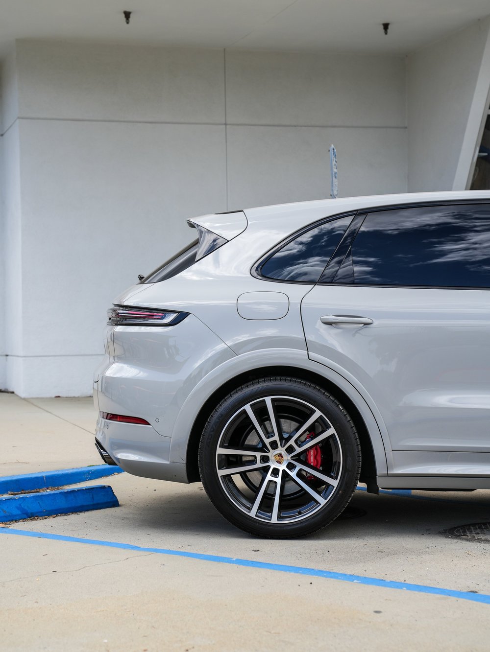 Light grey Porsche Cayenne GTS rear-quarter panel, taillamp and wheel against the workshop wall.