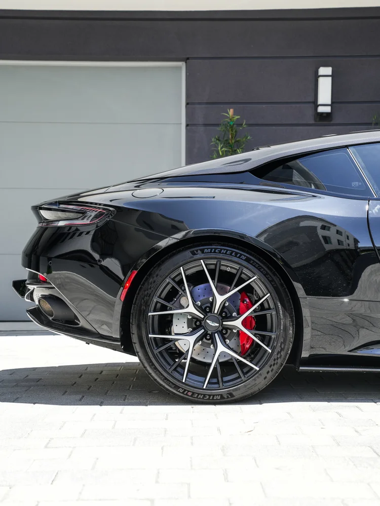 Rear wheel and red brake caliper beneath the reflective black DB12 rear quarter and tail lamp.