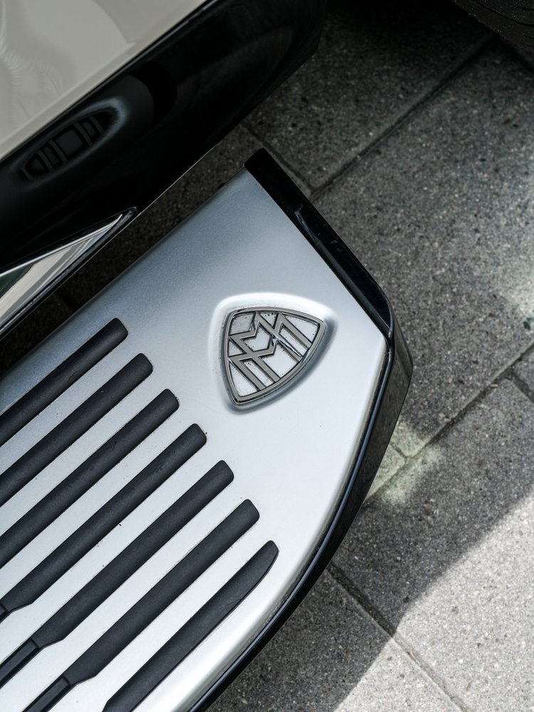 Maybach emblem on the silver exterior running board with black grip strips beside the white body.