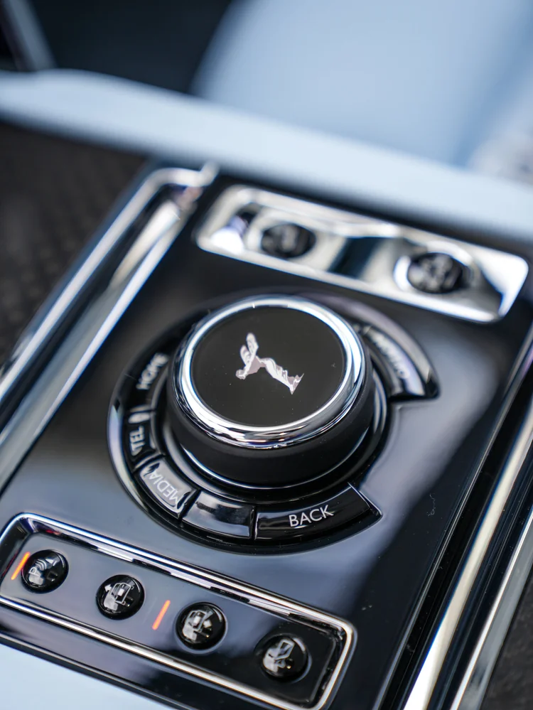 Cullinan center-console rotary controller with a Spirit of Ecstasy emblem and chrome switches beside pale upholstery