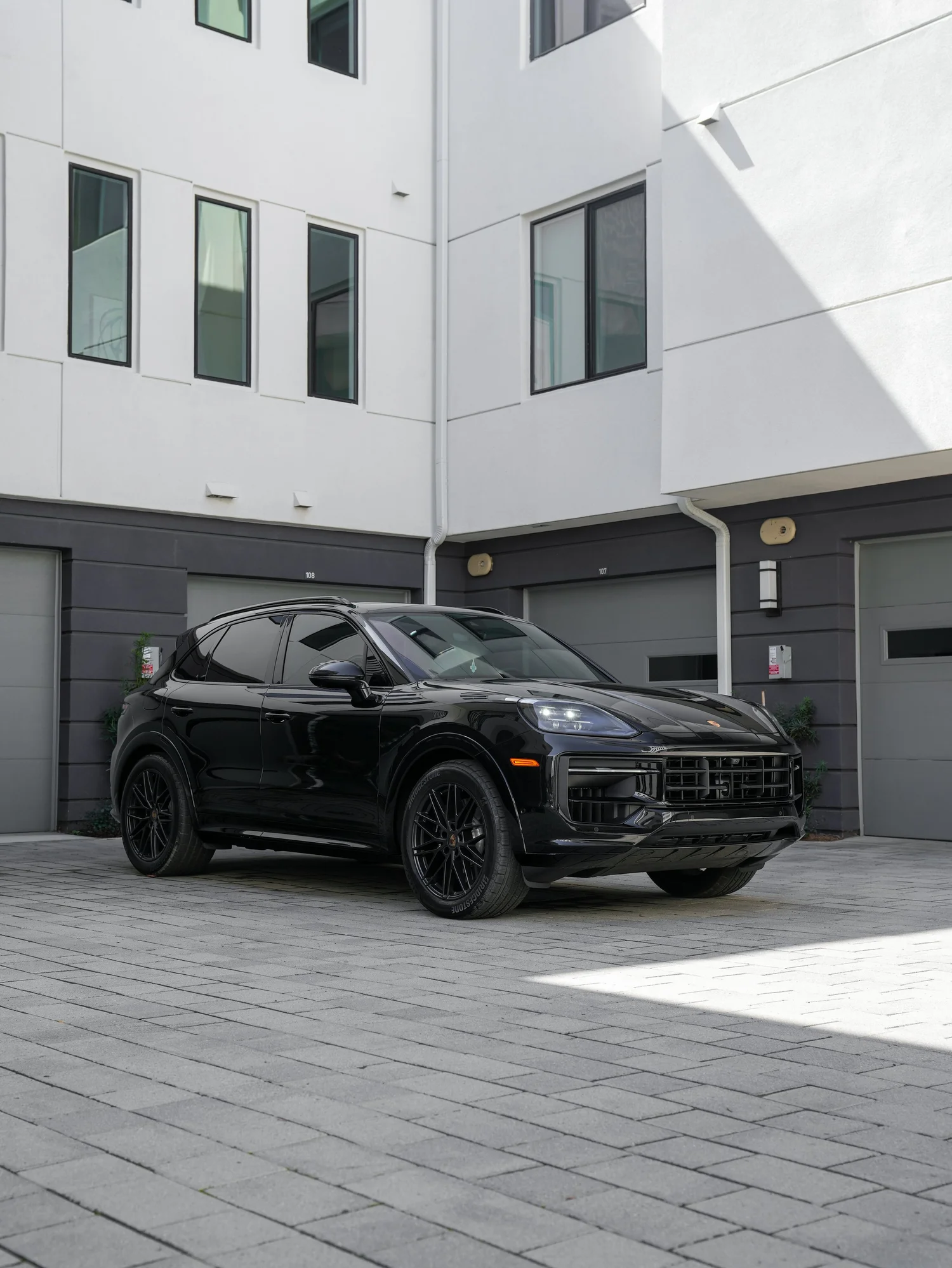 Complete front three-quarter view of the black Porsche Cayenne GTS with roof rails, mirrors, both visible wheels and full front bumper on paving.