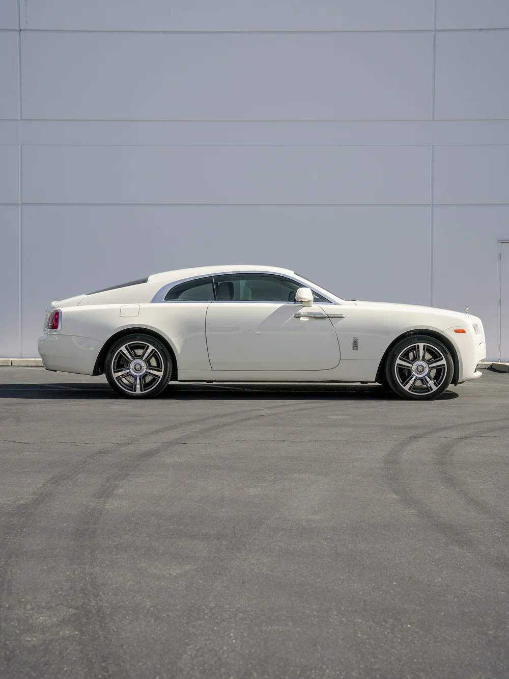 Complete side profile of the pale Rolls-Royce Wraith with both wheels and its sloping roofline.