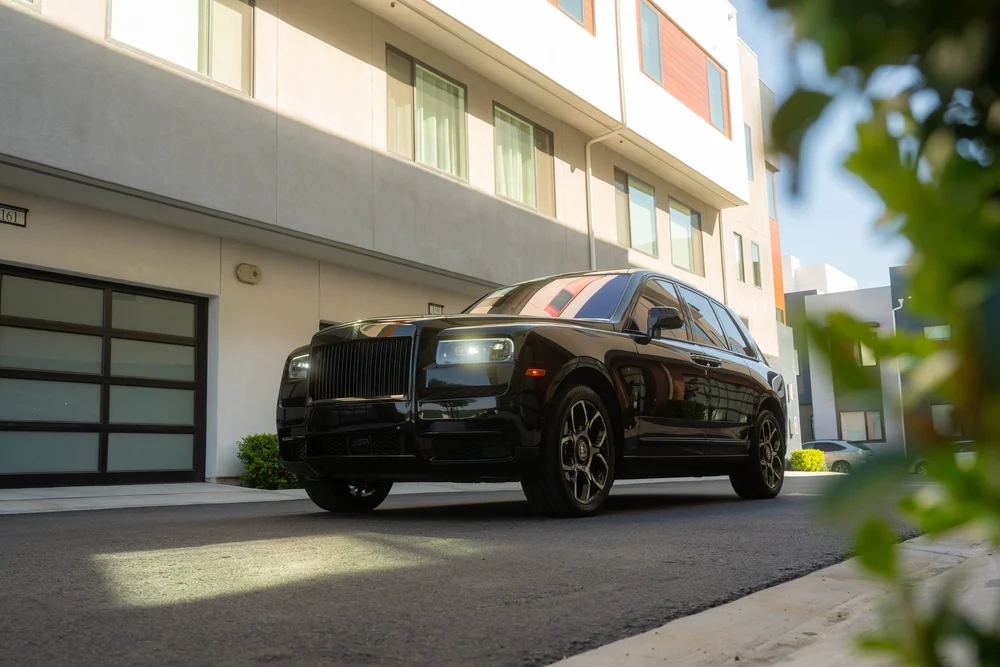 Black Rolls-Royce Cullinan Black Badge with Two-Tone Wheels — complete front three-quarter landscape view with foliage beside the vehicle