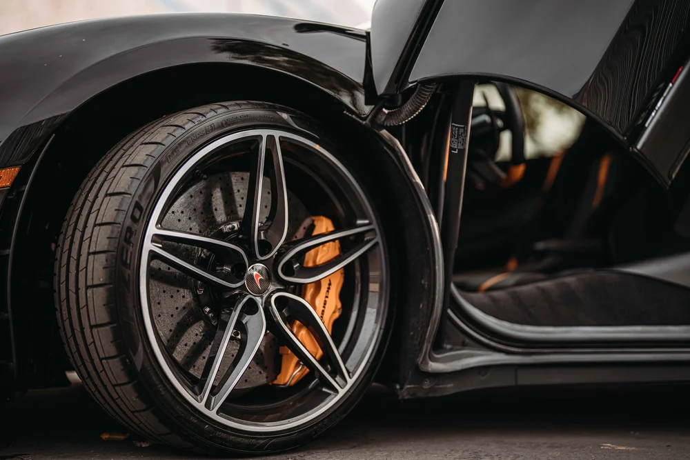 Wide wheel detail with the orange caliper, glossy fender and open doorway together in view.