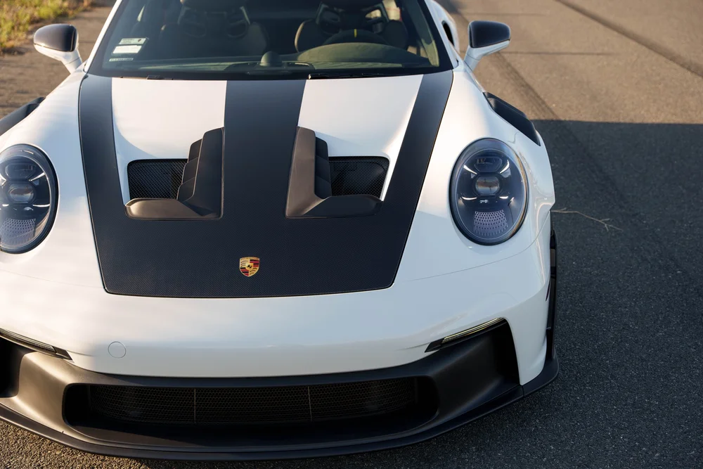 Elevated close view of the GT3 RS hood with a dark woven-texture center panel, vents, Porsche crest and white front bodywork