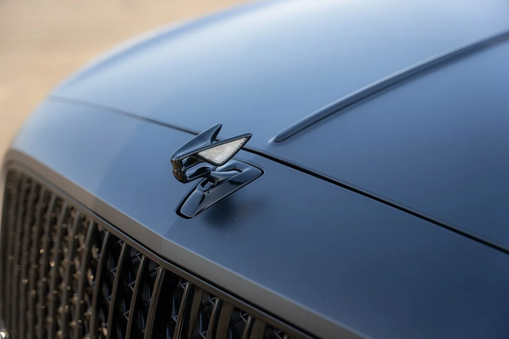 Raised winged hood ornament above the matte gray bonnet and black grille bars.