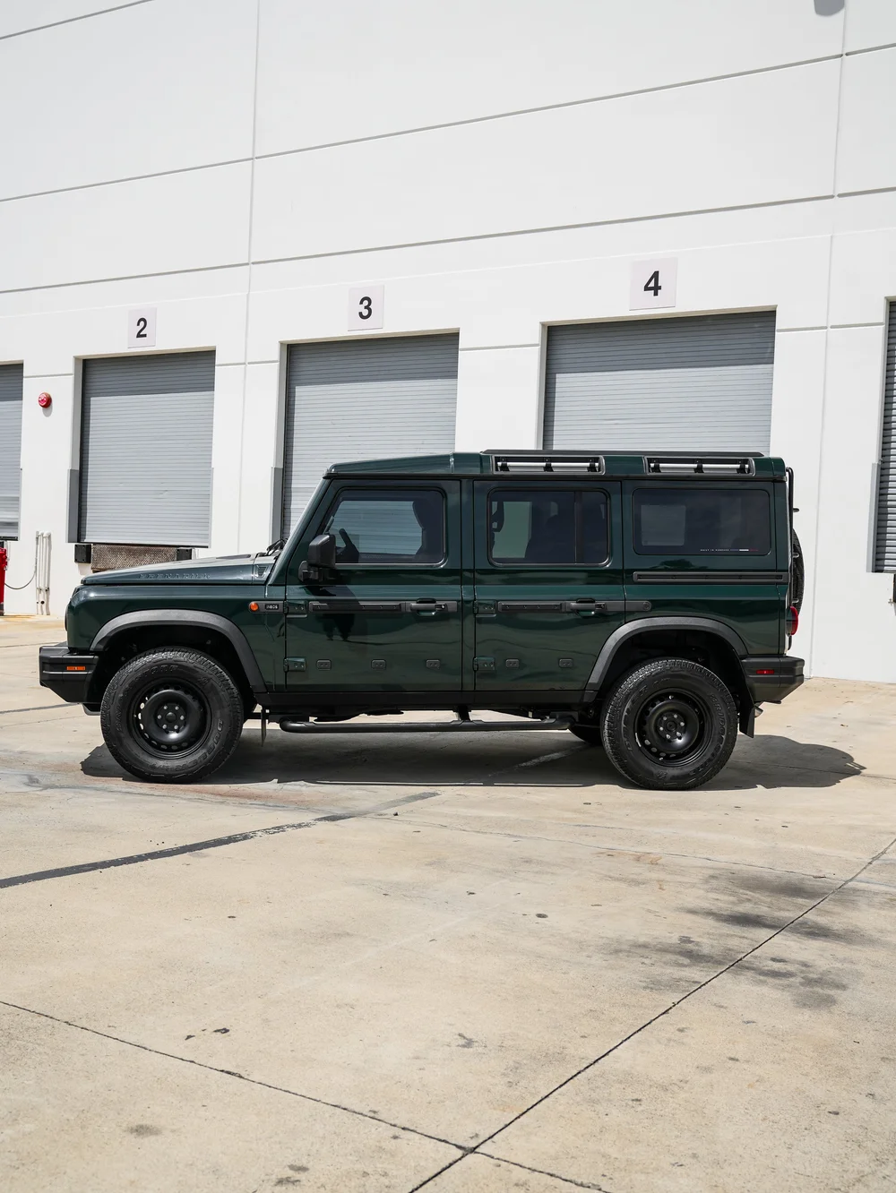 Full side profile of the green INEOS Grenadier with black wheels, roof rails and reflective side windows.